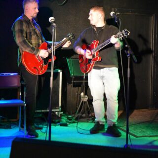 Två personer spelar gitarr ihop på en scen